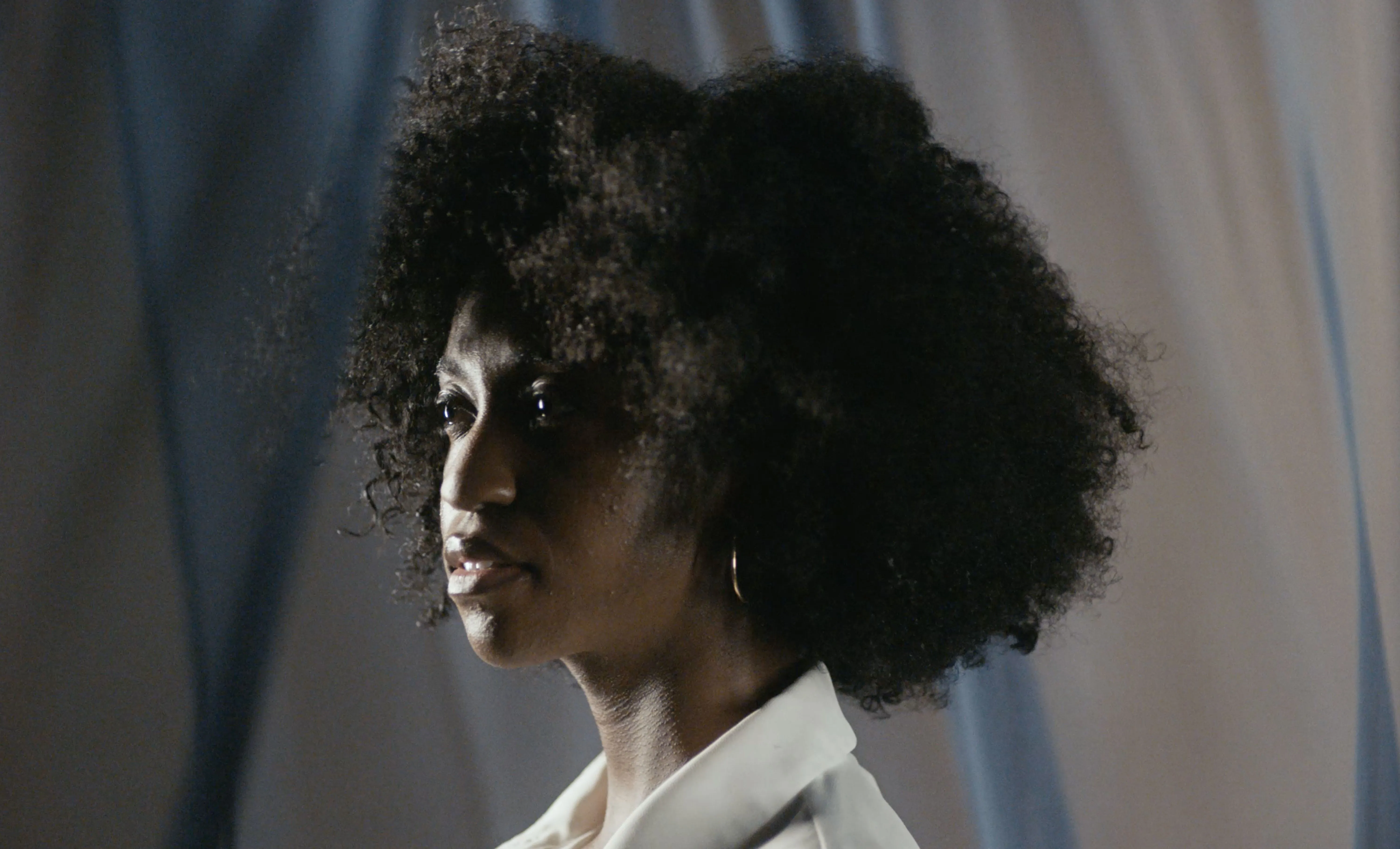 Female character in a Preamble film shown looking off-frame into the distance pensively.